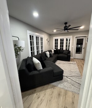 Una sala de estar moderna con un sofá modular, un ventilador de techo y un ventanal grande.