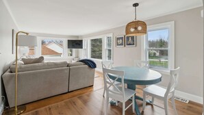 A modern living room with a sofa, a dining table with chairs, a floor lamp, and a hanging light fixture. - The Coastal Nest Stay for 5! (Scarborough)