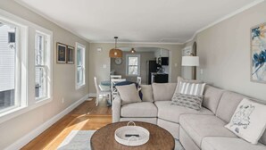 A living room with a beige sofa, a round coffee table, and a dining area in the background. - The Coastal Nest Stay for 5! (Scarborough)