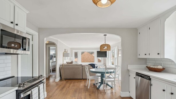 A modern kitchen with white cabinetry, a dining area with a round table and chairs, and a visible dishwasher. - The Coastal Nest Stay for 5! (Scarborough)