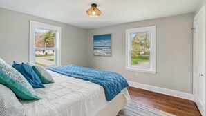 A bedroom with a bed, two windows, a painting, and a ceiling light. - The Coastal Nest Stay for 5! (Scarborough)