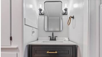 A bathroom with a white vanity, a dark cabinet below, a mirror above the sink, and two wall-mounted light fixtures.