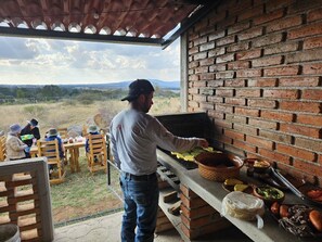A person grilling food outdoors with a brick wall and a view of the countryside. - Cabañas El Campo (Amealco)