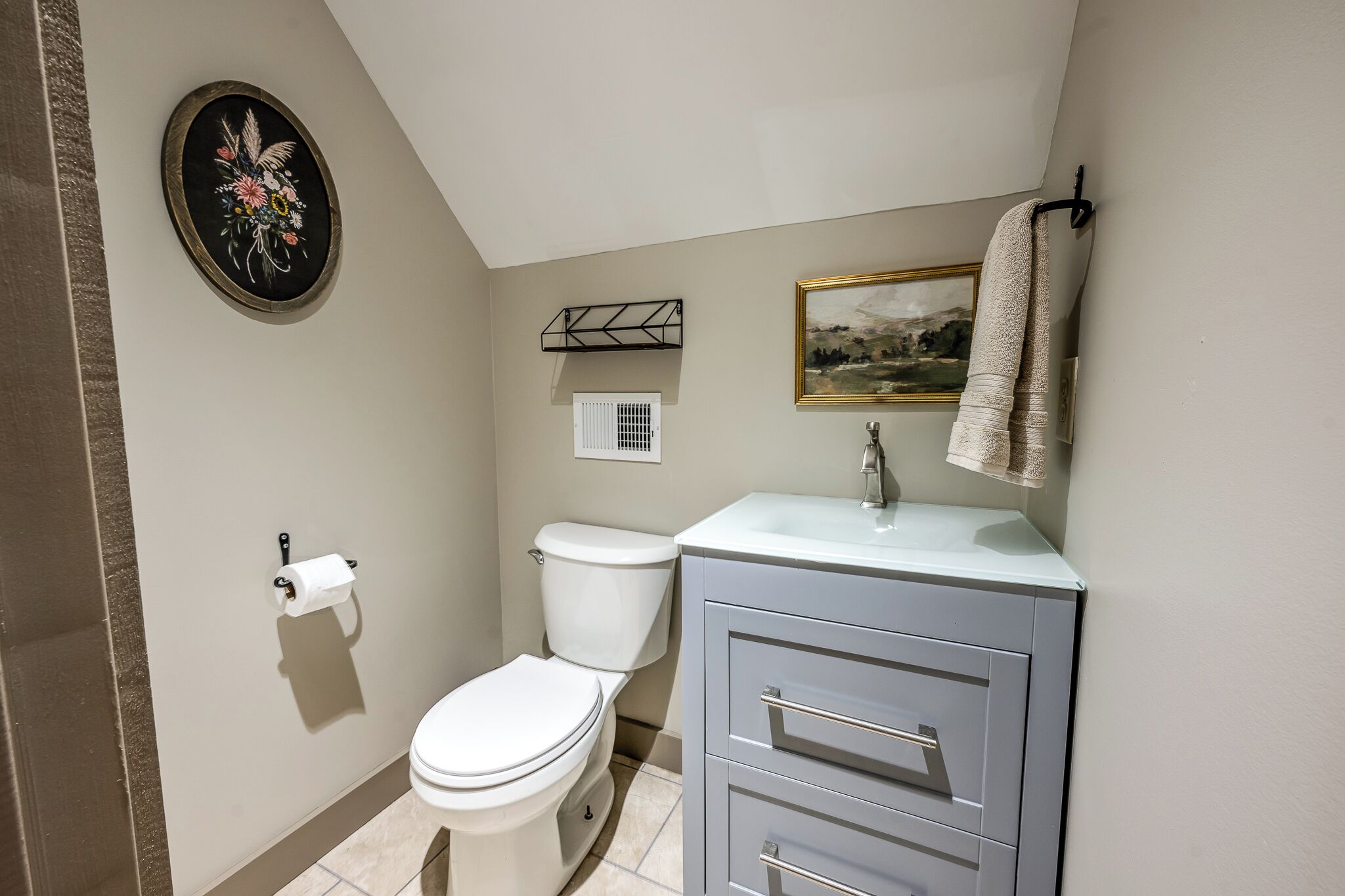 A bathroom with a toilet, a sink, a towel rack, a framed picture, and a decorative item on the wall.