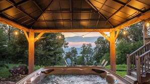 Un bain à remous sous une pergola en bois, avec vue sur les arbres et un coucher de soleil.