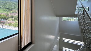 Un intérieur moderne avec un escalier, une grande fenêtre avec des rideaux et une vue sur la verdure et les bâtiments environnants.