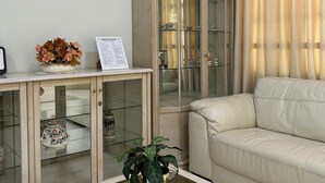 Un salon avec une table basse à plateau de verre, un canapé beige, un meuble vitré et une plante en pot.
