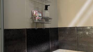 A shower with a handheld showerhead, a soap dispenser, and a soap bar on a metal shelf.