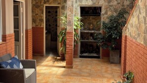 A covered outdoor area with a brick wall, tiled floor, and a wicker chair. - CASA LUNA - Complete lodging (Salta)