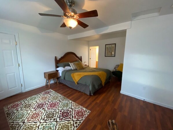 A bedroom with a wooden floor, a bed with a headboard, a nightstand, a ceiling fan, and a door. - Charming Room 3 in the St. Maries Inn (Saint Maries)