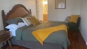 Une chambre à coucher avec un lit en bois, une literie verte, un plaid jaune, une table de chevet et une chaise avec un coussin jaune.