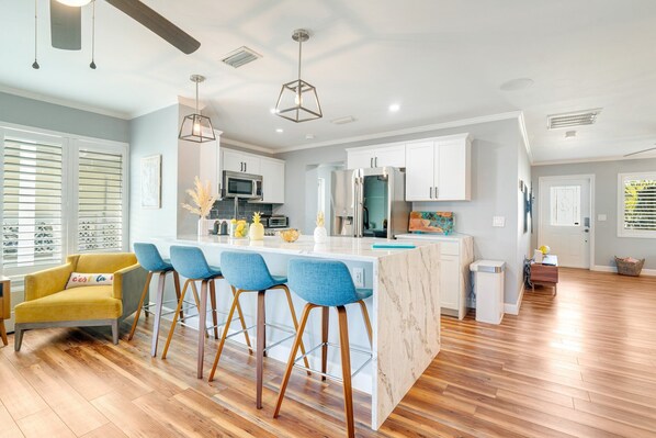 A modern kitchen with a central island, bar stools, and a yellow armchair.