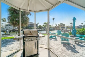 Un espacio al aire libre techado con una parrilla, asientos y vistas a un puerto deportivo.