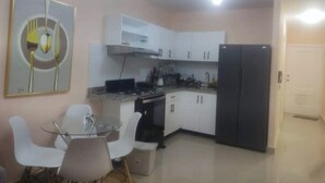 A compact kitchen with white cabinets, a black refrigerator, and a dining area with a glass table and white chairs. - A place of relaxation and disconnection (Boca Chica)
