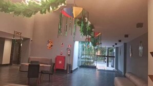 A spacious lobby with a modern design, featuring a reception desk, seating area, and decorative elements like hanging ornaments. - Apto 00203 Legacy Suites  (João Pessoa)
