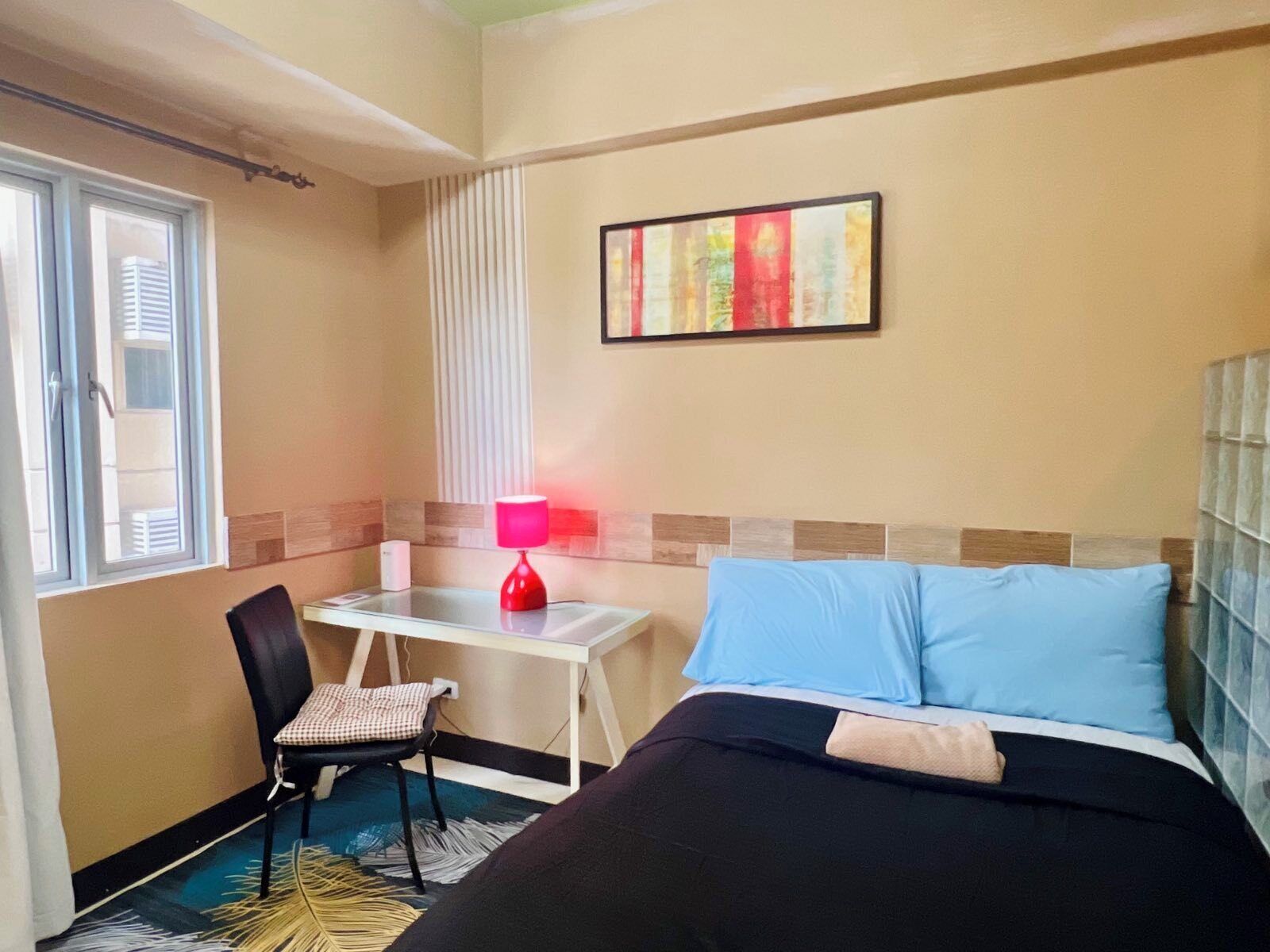 Een hotelkamer met een bed, een bureau, een stoel, een raam en een schilderij aan de muur.