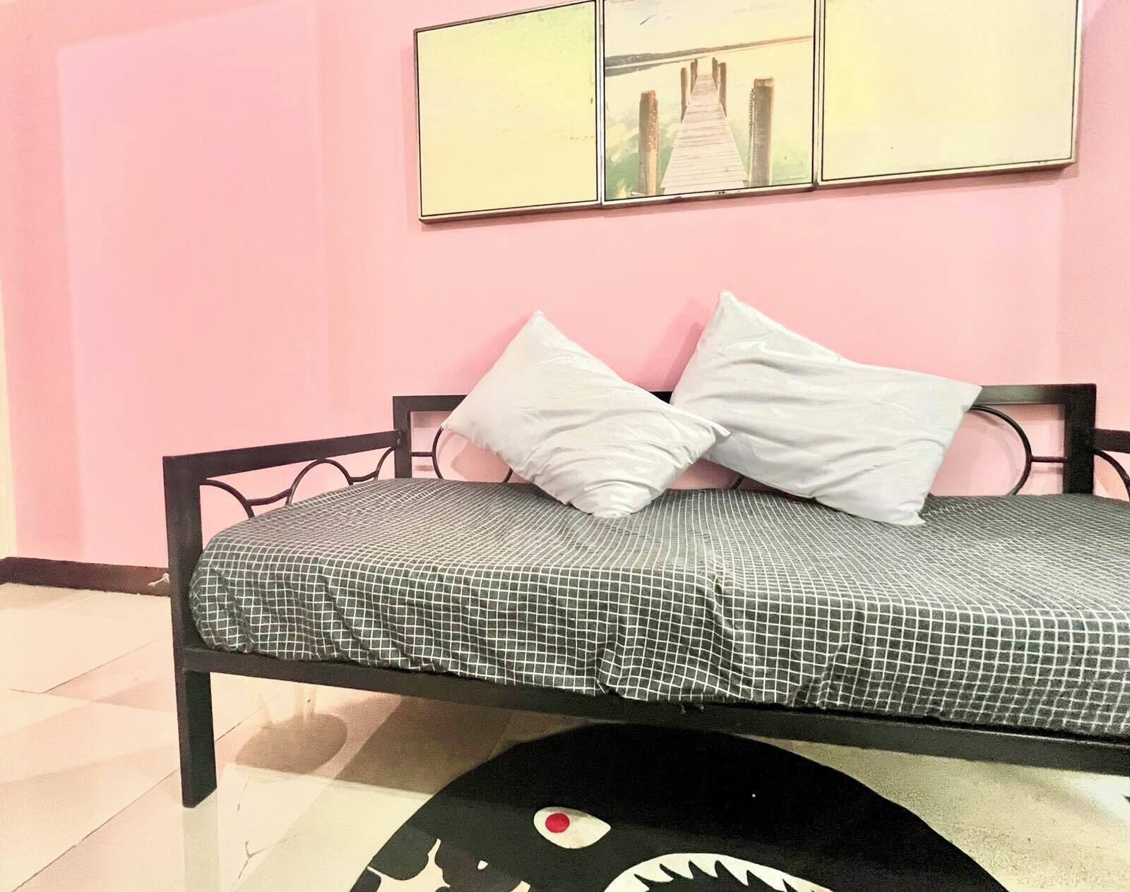 A single bed with a checkered bedspread, two white pillows, and a black and white rug with a fish design.