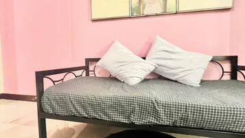 A single bed with a checkered bedspread, two white pillows, and a black and white rug with a fish design.