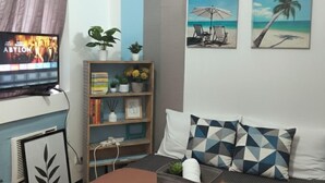 Een moderne slaapkamer met een bed, een televisie, een boekenkast en twee schilderijen met een strandthema.