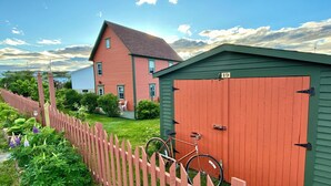 Une grange rouge avec un toit vert, un vélo garé devant et une clôture blanche entourant la propriété.