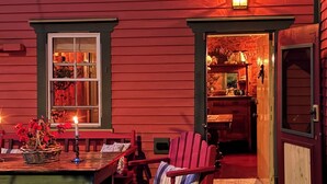 Une terrasse en bois avec une table et des chaises, un panier rempli de fleurs et une porte donnant sur un espace intérieur.