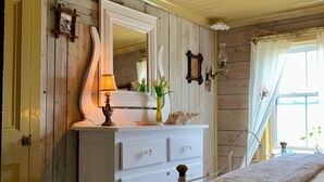 Une chambre avec une commode blanche, un miroir, une lampe et une fenêtre avec des rideaux.
