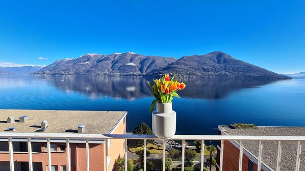 Un balcón con un jarrón de tulipanes con vistas a un lago tranquilo y montañas.