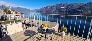 Un balcón con una mesa dispuesta para una comida, con vistas a un lago y montañas al fondo.