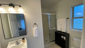 Un baño con lavamanos blanco, espejo, toallero, cabina de ducha e inodoro.