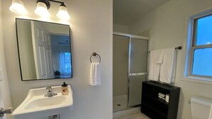 Un baño con lavamanos blanco, un espejo, un mueble negro, un inodoro y una zona de ducha.
