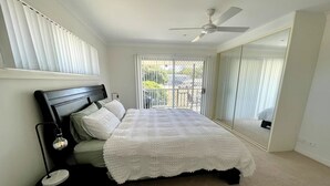 A bedroom with a bed, a nightstand, a ceiling fan, and a view through a window. - Anna Bay Beachside Getaway (Anna Bay)