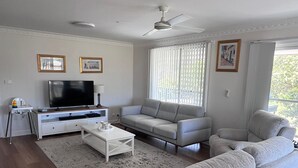 A modern living room with a grey sofa, a white coffee table, and a flat-screen TV. - Anna Bay Beachside Getaway (Anna Bay)