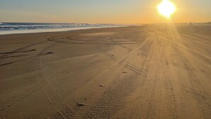 A beach with tire tracks and a sunset in the background. - Anna Bay Beachside Getaway (Anna Bay)