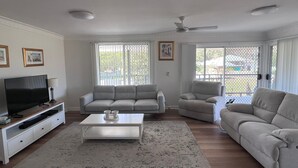 A living room with a TV, sofas, a coffee table, and a ceiling fan. - Anna Bay Beachside Getaway (Anna Bay)