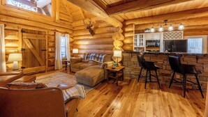 L’intérieur d’une cabane en rondins présente un espace de vie chaleureux, un mur d’accent en pierre et une cuisine équipée d’appareils électroménagers modernes.