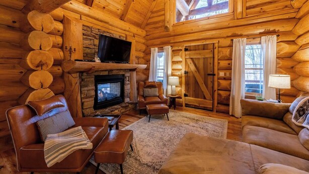 L’intérieur d’une cabane en rondins, avec une cheminée en pierre, des meubles en cuir et un téléviseur.