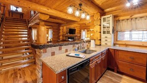 L’intérieur d’une cabane en rondins présente une cuisine équipée d’un plan de travail en granit, de meubles en bois et d’un lave-vaisselle encastré.