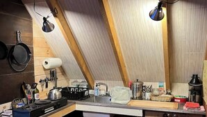 Una cocina compacta con techo inclinado, vigas de madera, estufa a gas, pileta y diversos utensilios de cocina.