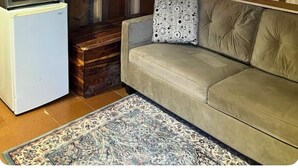Una habitación acogedora en el ático con techo de madera, un refrigerador blanco, un sofá color beige y una alfombra estampada.