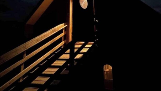 Un pequeño edificio con techo oscuro y una escalera de madera que lleva a una puerta.