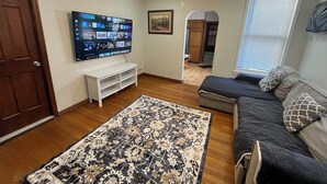A living room with a flat-screen TV, a patterned rug, a dark-colored sofa, and a ceiling fan.