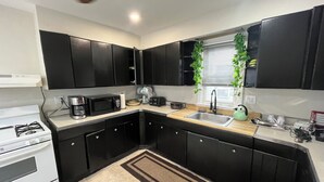 A compact kitchen with black cabinets, a white stove, a microwave, a sink, and a window with a plant.
