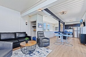 A modern living room with a black leather sofa, a round coffee table, and a gray armchair. A kitchen area is visible in the background with a dining table and bar stools. - Awesome Custom Built Home.  Perfect Indy Location! (Indianapolis)