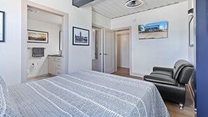 A bedroom with a bed, a black leather chair, a bathroom with a toilet and sink, and a hallway with doors leading to other rooms.
