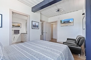 A bedroom with a bed, a black leather chair, a bathroom with a toilet and sink, and a hallway with doors leading to other rooms. - Awesome Custom Built Home.  Perfect Indy Location! (Indianapolis)