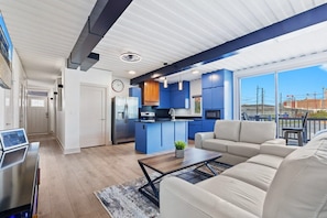A modern kitchen with blue cabinets, a central island, and a dining area with a sofa and coffee table. - Awesome Custom Built Home. Perfect Indy Location! (Indianapolis)