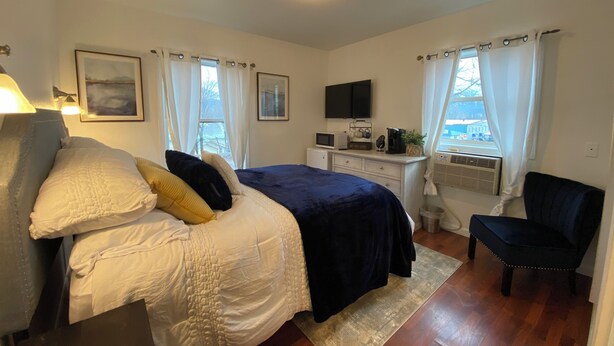 A bedroom with a bed, a desk with a computer, a chair, and a window with curtains. - Charming Room 5 in the St. Maries Inn (Saint Maries)
