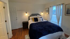 A bedroom with a bed, bedside tables, a nightstand, a door, and a window with curtains. - Charming Room 5 in the St. Maries Inn (Saint Maries)