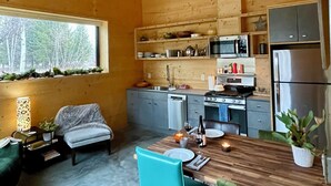 A modern kitchen with wooden walls, a dining area with a wooden table and chairs, and a window with a view of trees.