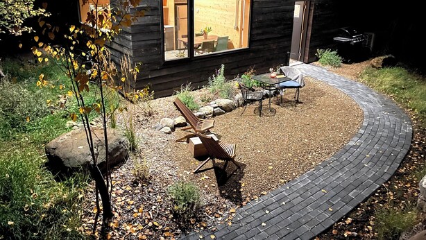 A modern log cabin with a curved brick pathway leading to a seating area with a table and chairs.